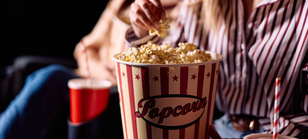 People enjoying a movie night, eating popcorn and drinking soda in a dark theater, experiencing entertainment and leisure